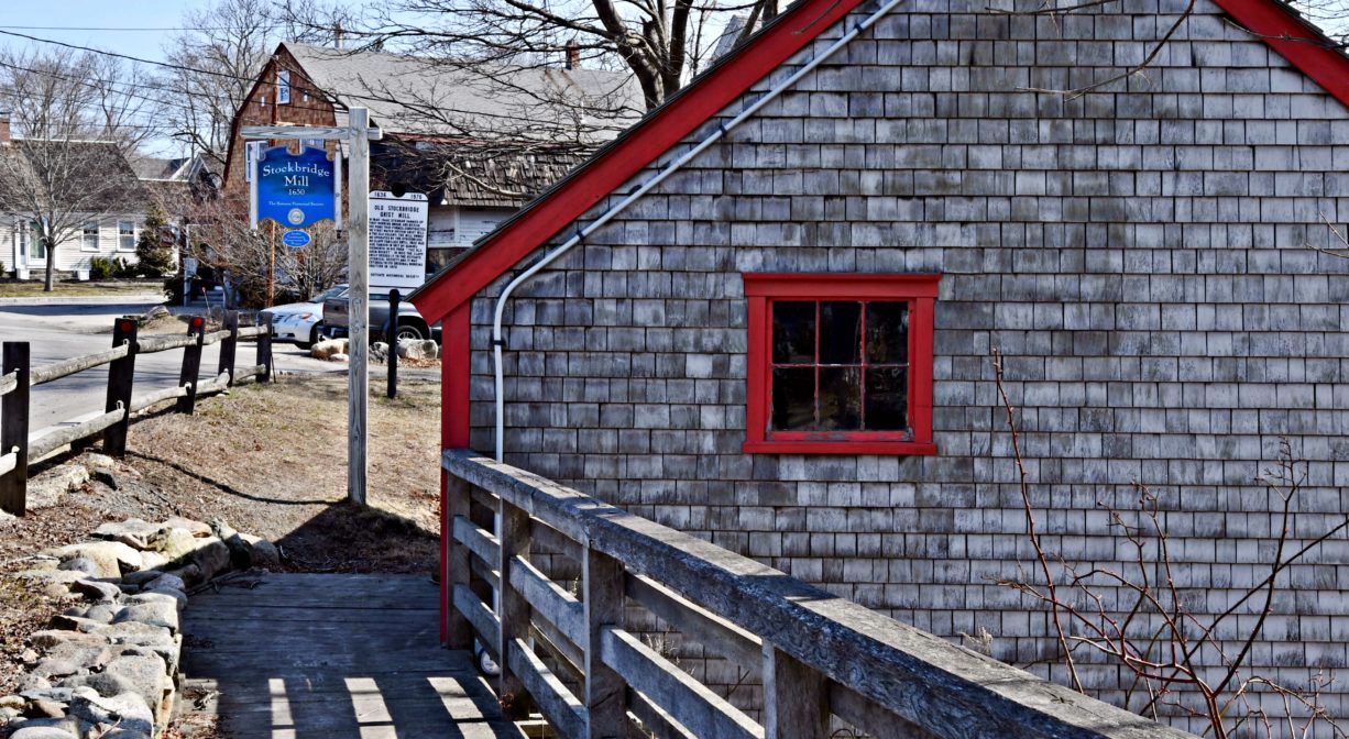 A photograph of a shingled mill building and a property sign.
