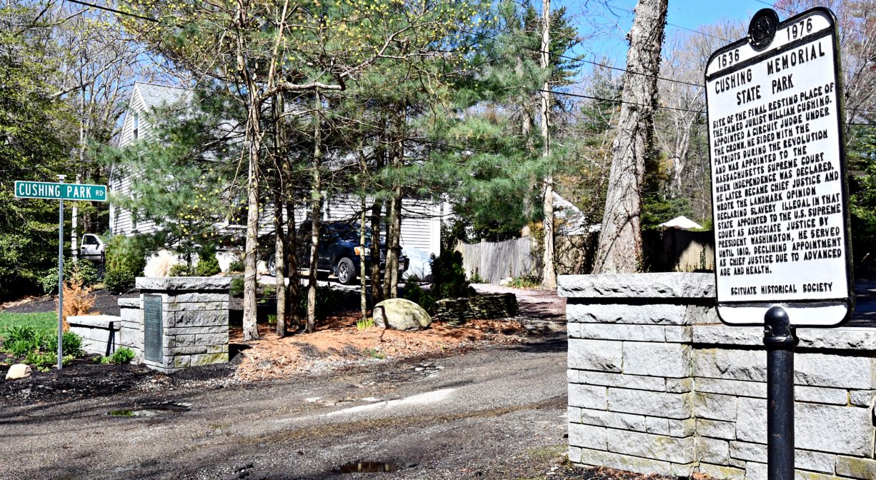 A historical marker and a granite wall with a roadway in between.