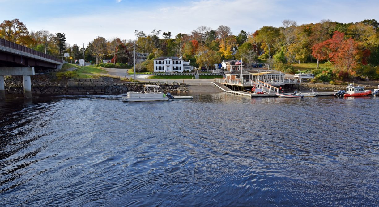 A photograph of a river with a marina in the background and bridge to one side.