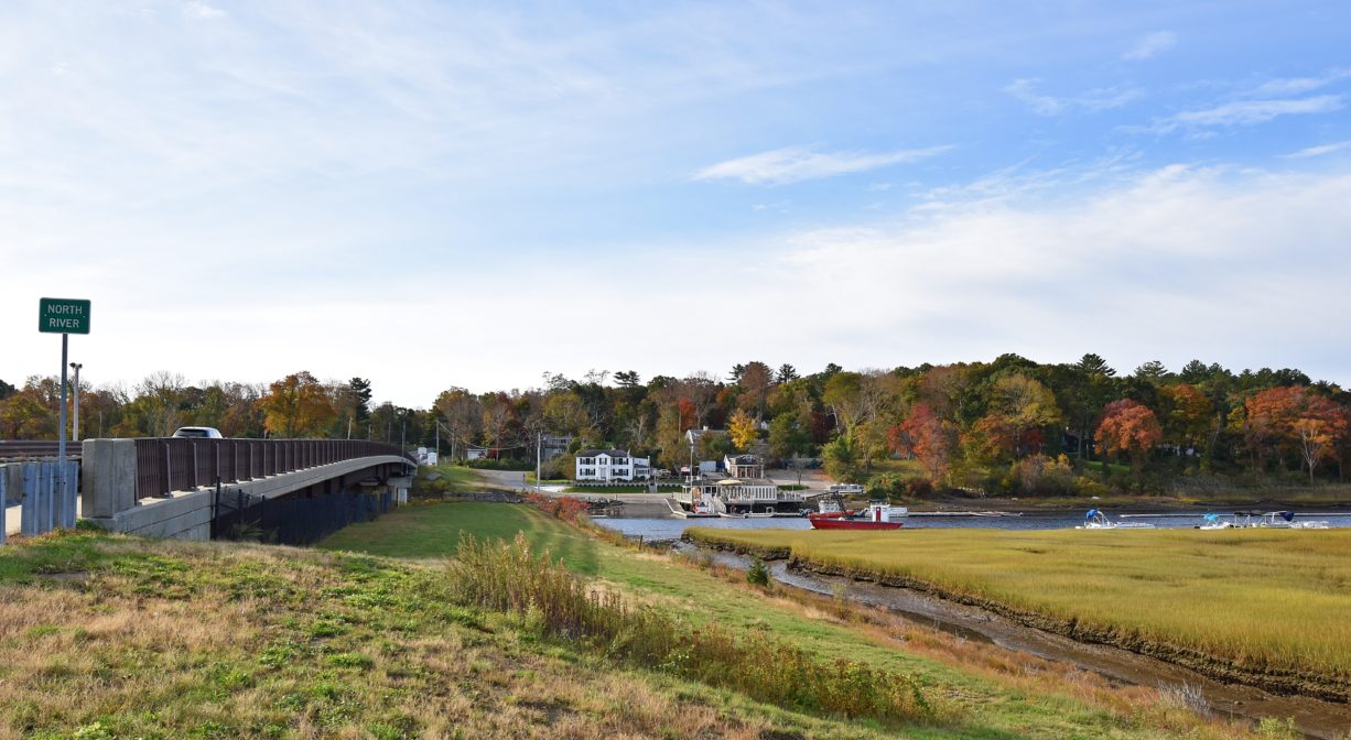 A photograph of a distant view of a marina on a river.