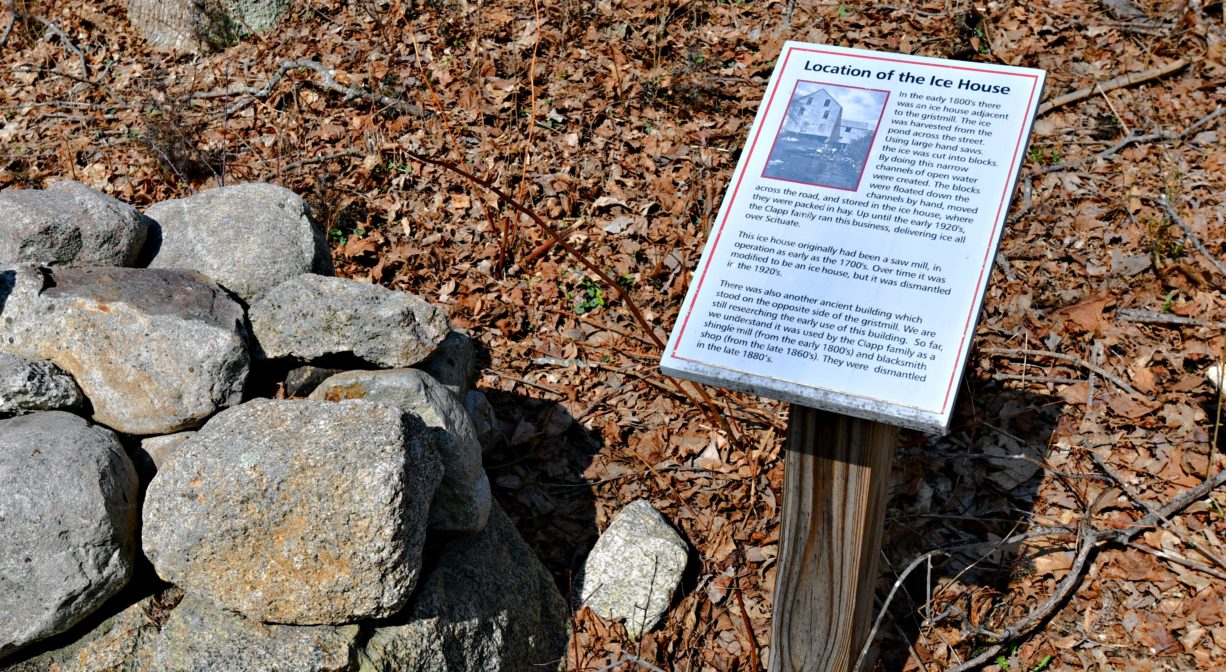 A photograph of an interpretive sign and a stone wall with fall leaves.