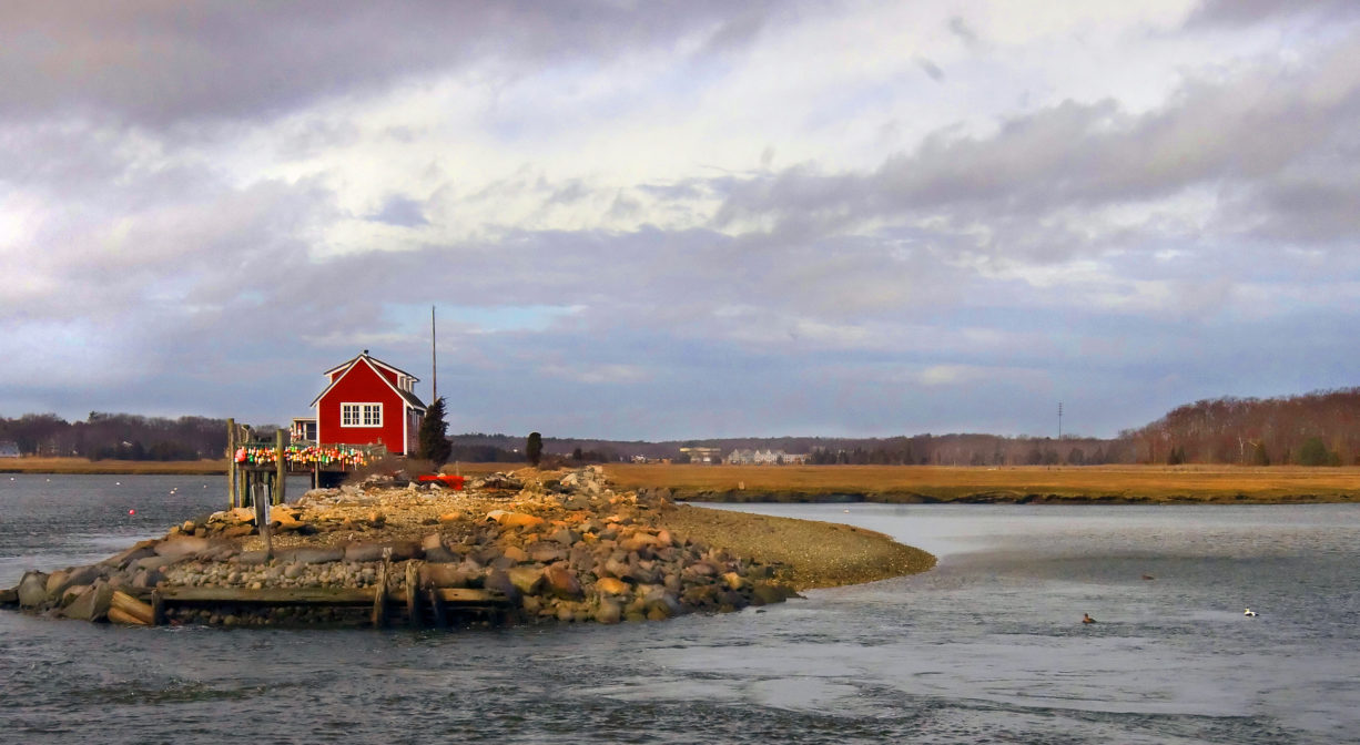 A red cottage perched atop a former railroad bed, at the edge of a river and salt marsh.