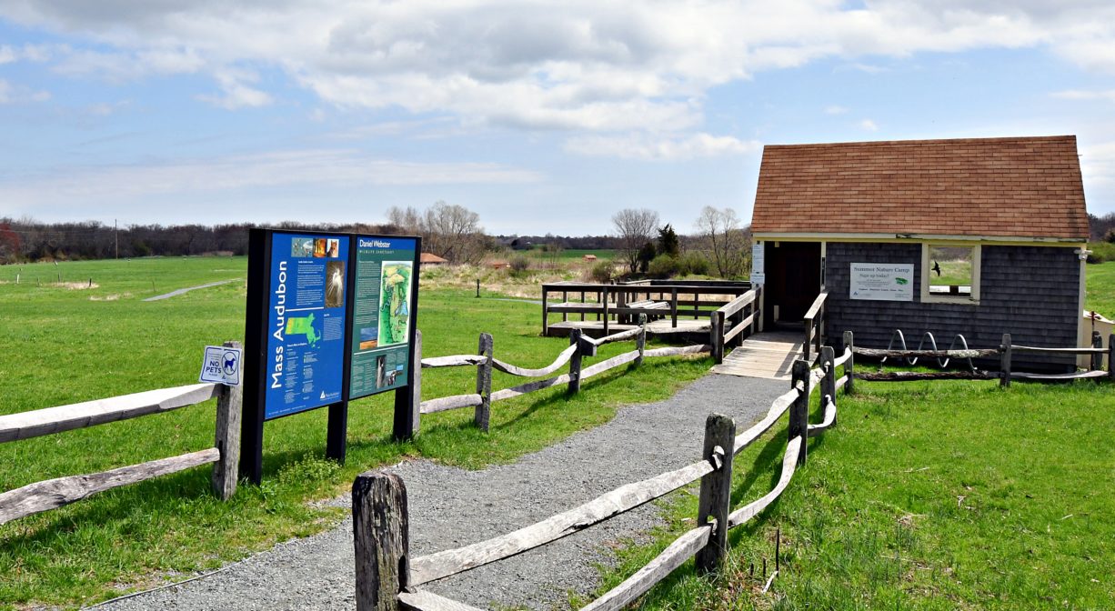 A photograph of a entrance trail and building, on a grassy green landscape.
