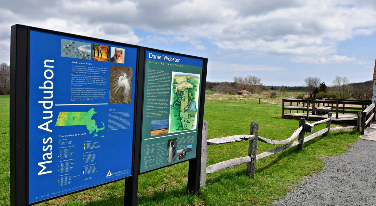 A photograph of interpretive signage along an entrance trail on a grassy green landscape.