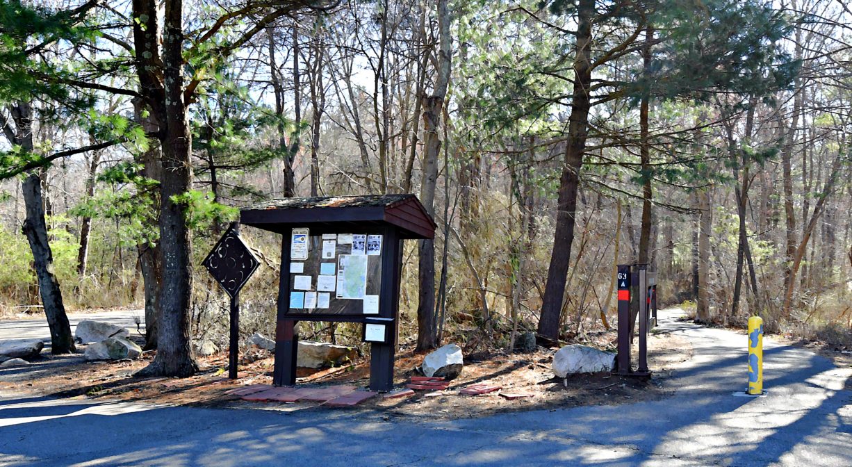 A photograph of an informational kiosk beside a paved trail, with a woodland in the background.