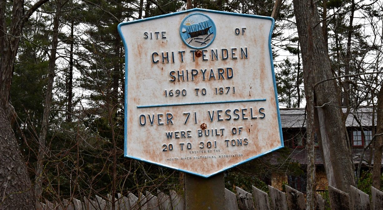 A photograph of a historic marker with trees and marsh grass in the background.