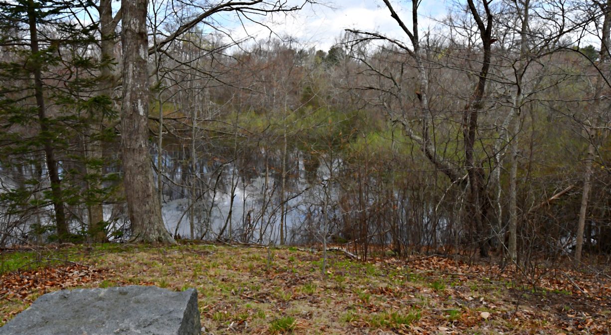 A photograph of a granite block bench on a grassy hill overlooking a pond.