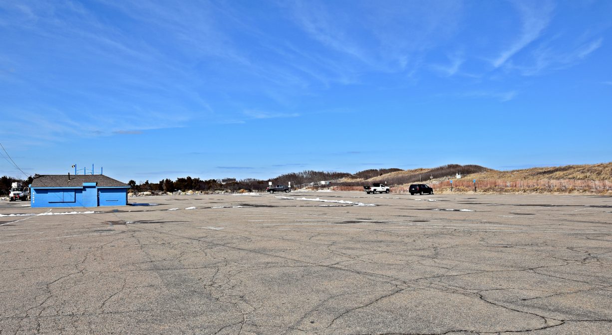 A photograph of a large paved parking lot with a small blue building to one side.