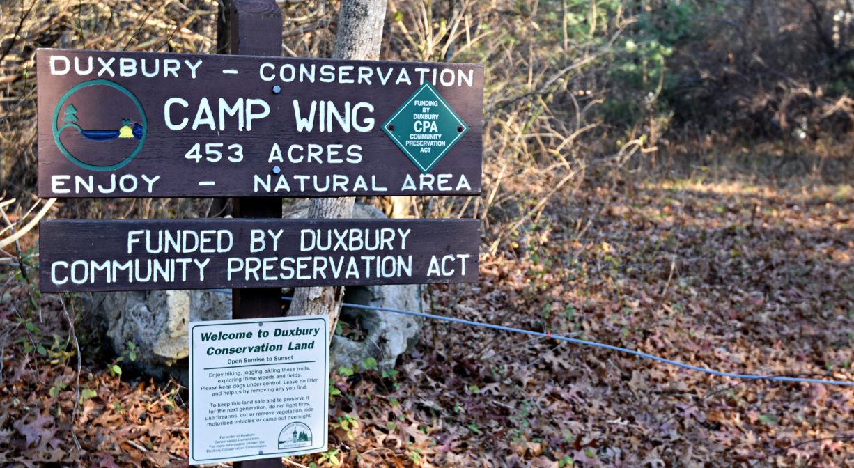A photograph of a property sign and a trailhead with a forest in the background.
