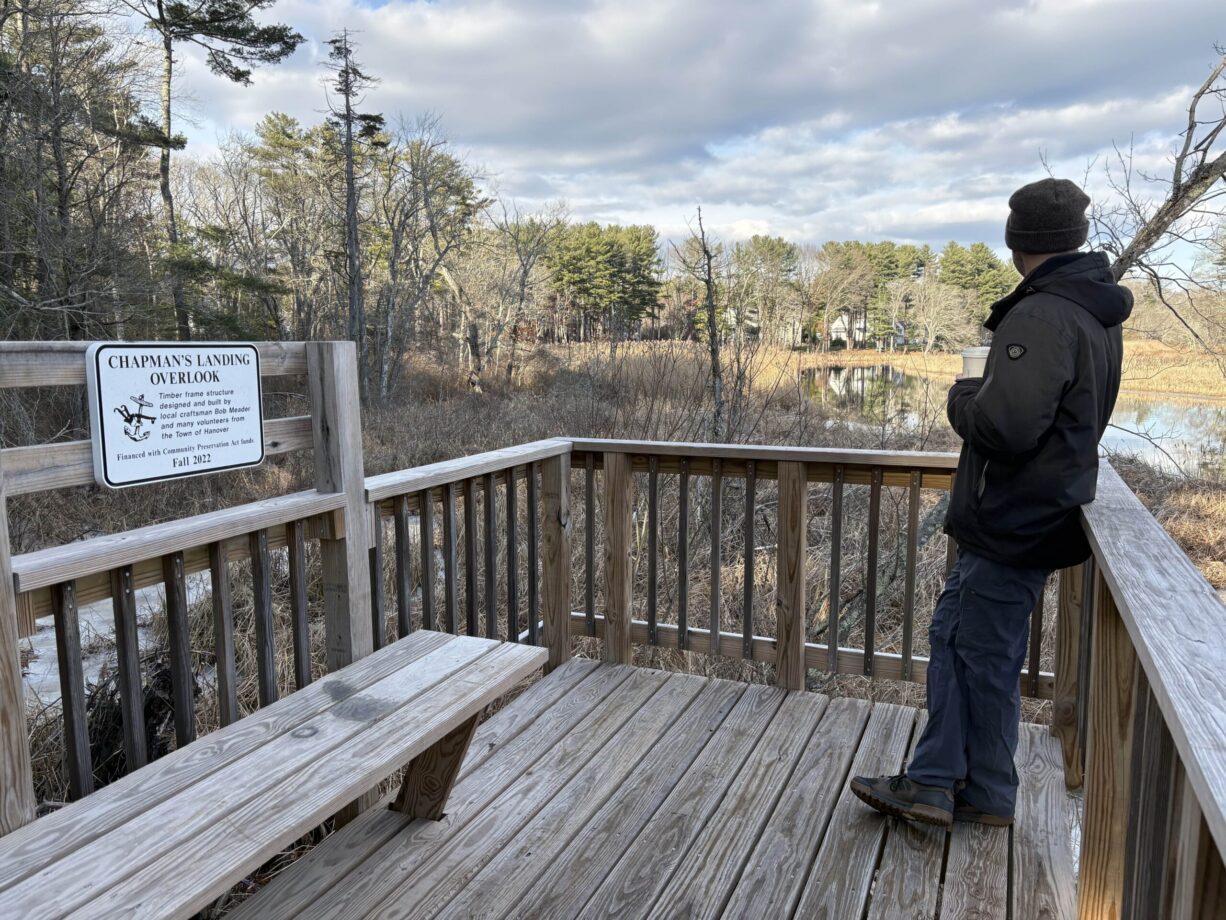 A photograph of an individual looking out a a river and marsh from a raised wooden platform.