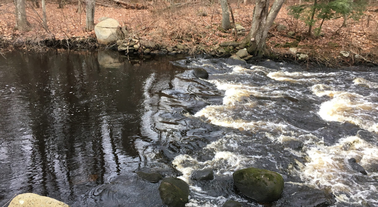 A photograph of a river flowing over an old dam.