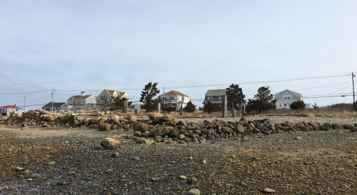 A photograph of a stone foundation on the beach with a low tidal area in the foreground.