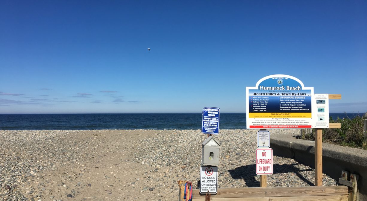 A property sign with a beach in the background.