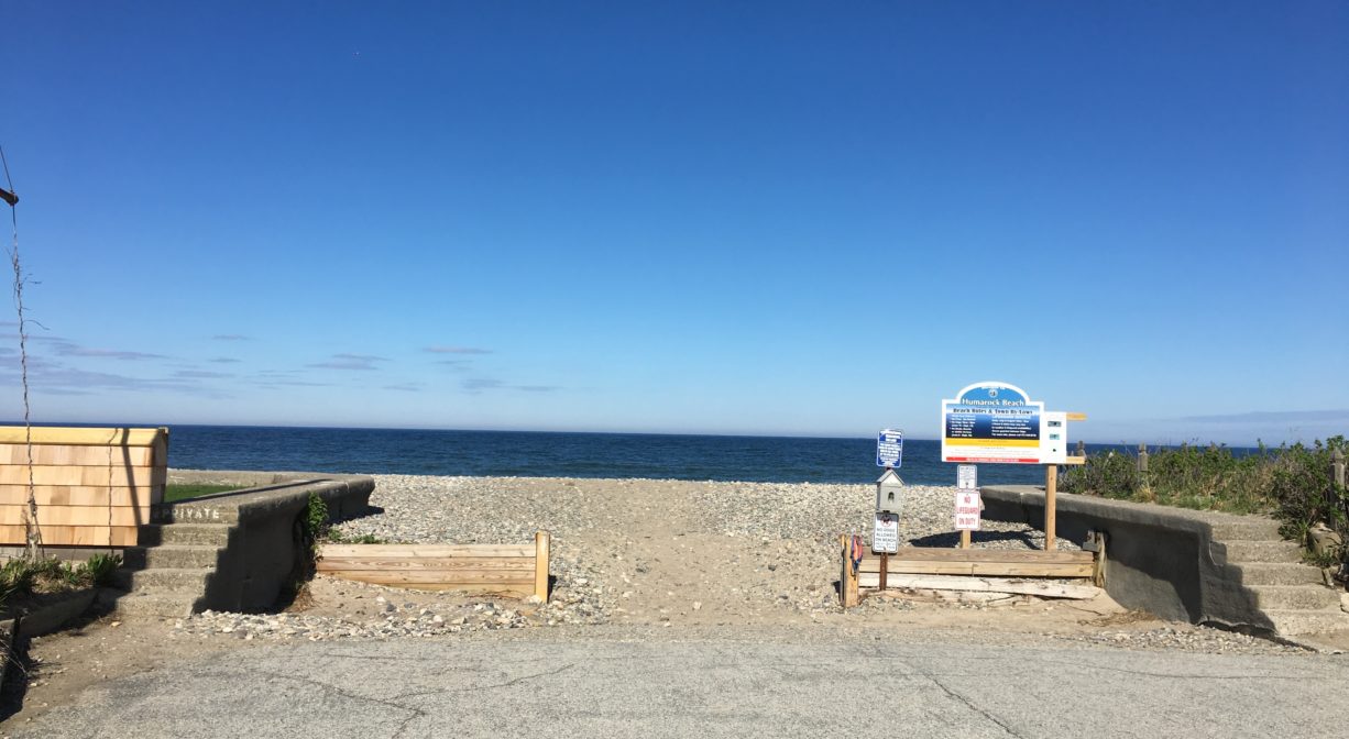 An entrance to a beach with sea walls on both sides and a property sign.