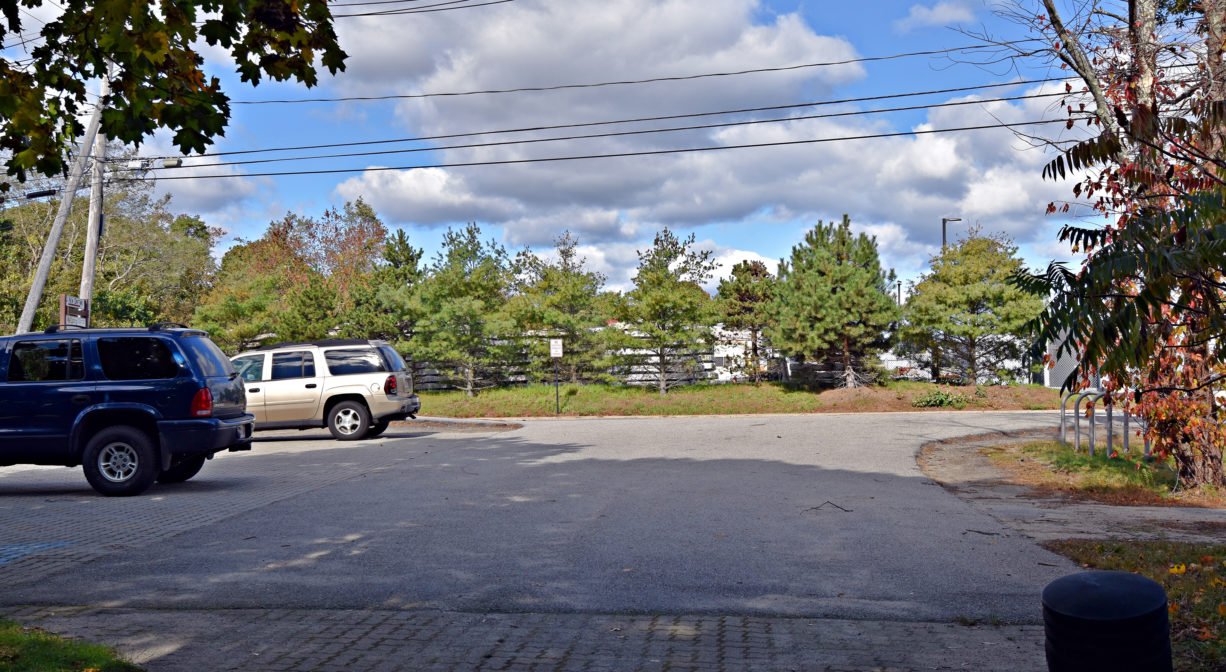 Photograph of a parking area with two vehicles plus some trees in the background.