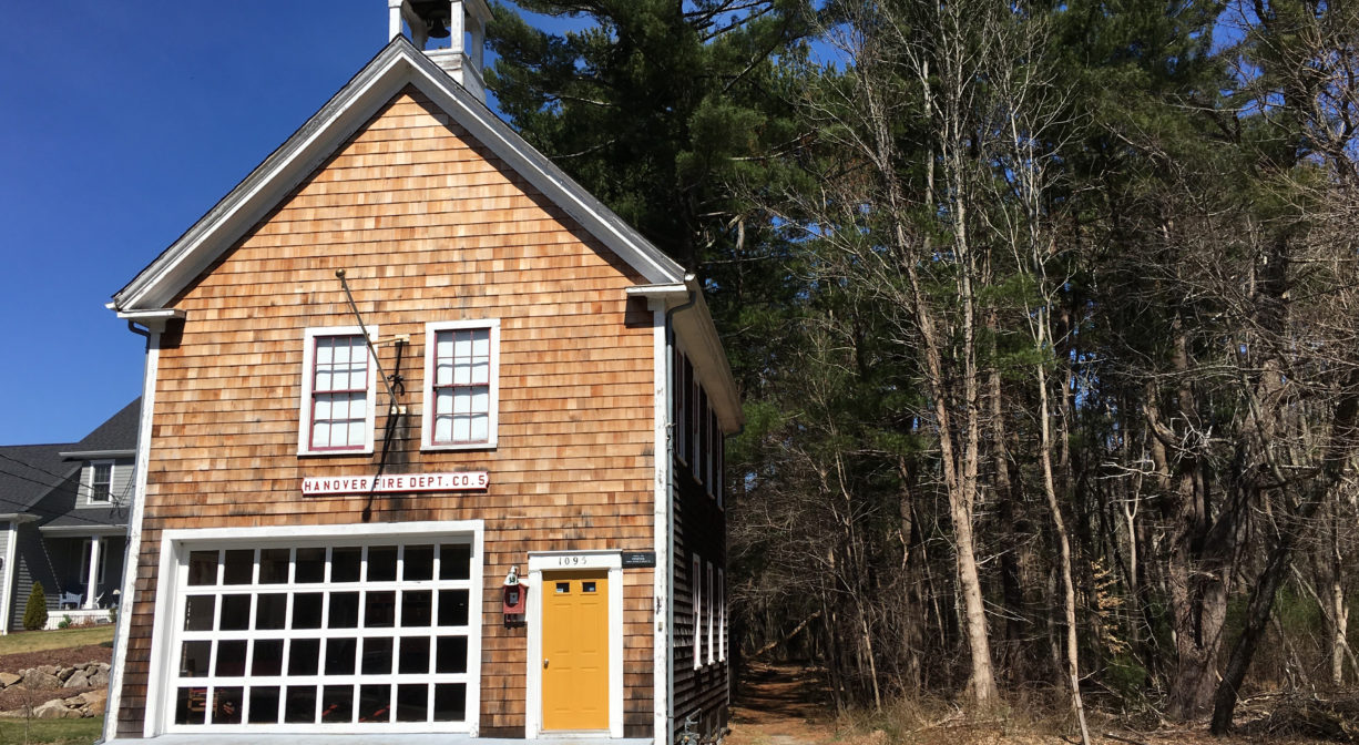 A photograph of a restored firehouse with a forest trailhead beside it.