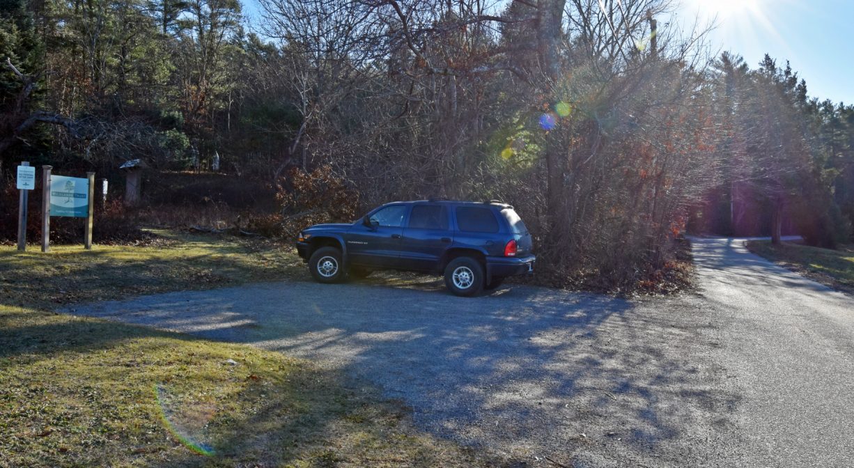 A photograph of a small parking area with a trailhead and two property signs.