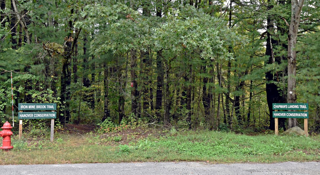 A photograph of a two trailheads and two trail signs, with green foliage.