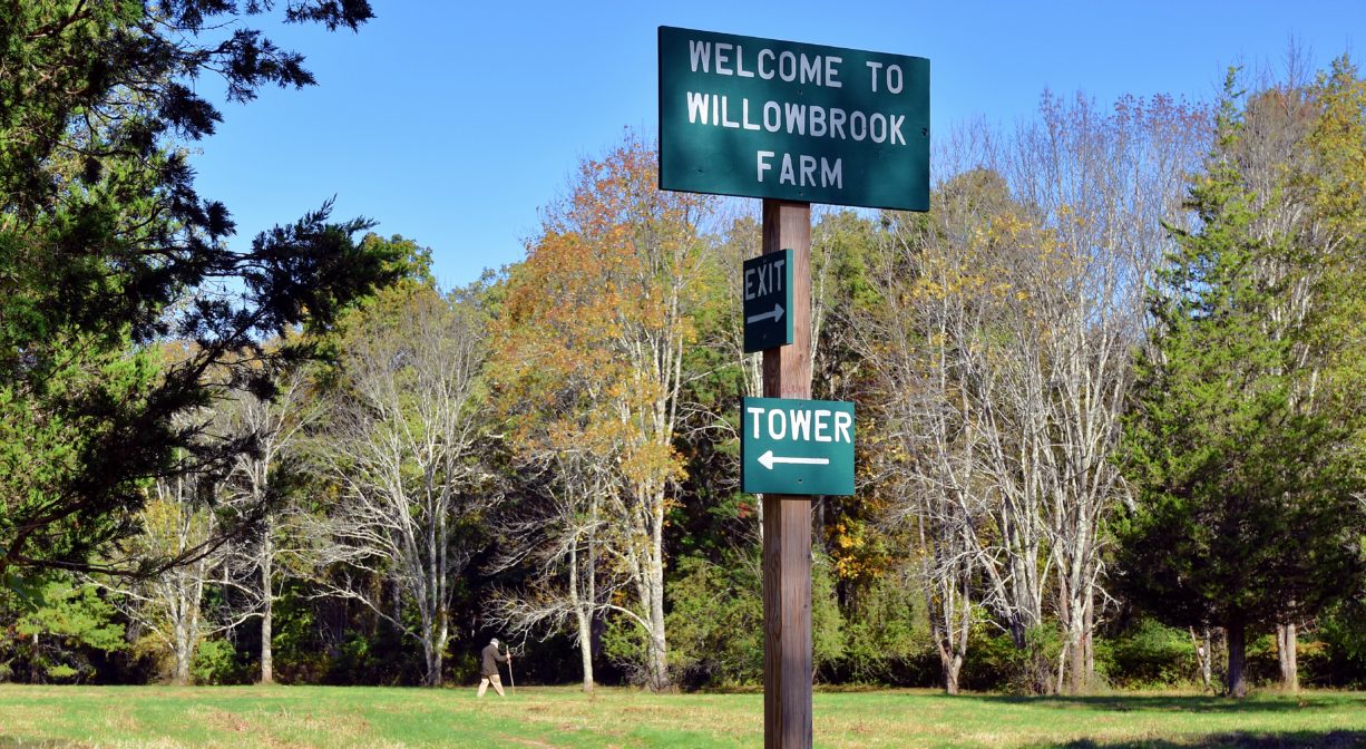 A photograph of a property sign with trees and a grassy field in the background.