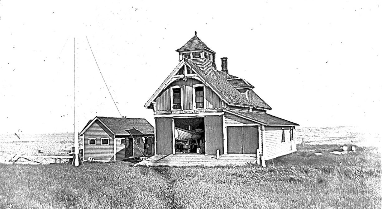 Historic black & white image of a wooden 2-story cottage with a pole on the waterfront side of the property.