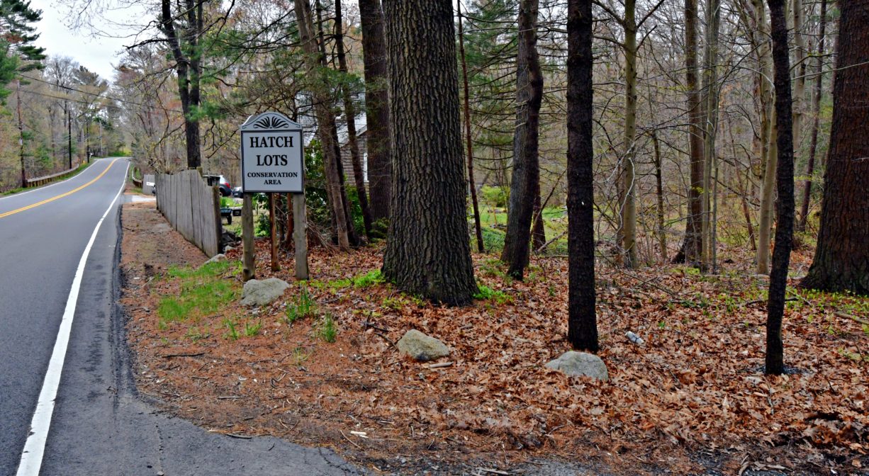 A photograph of a property entrance with a sign and a forest.