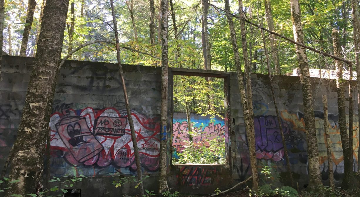 Photograph of an abandoned concrete building in a forested setting, with some graffiti.