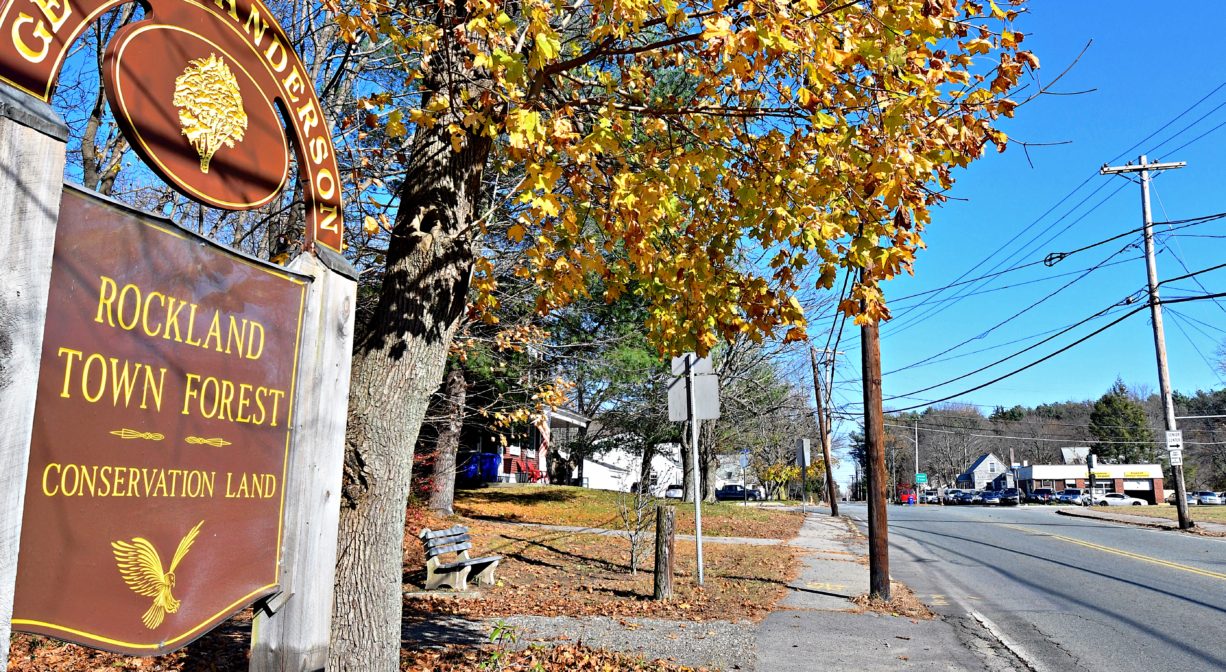 Photograph of brown property sign at edge of roadway with some fall foliage.