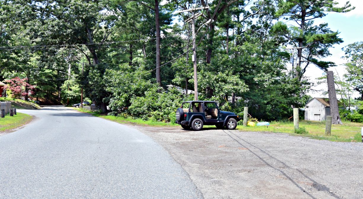 A photograph of a parking area with a jeep, with trees in the background.