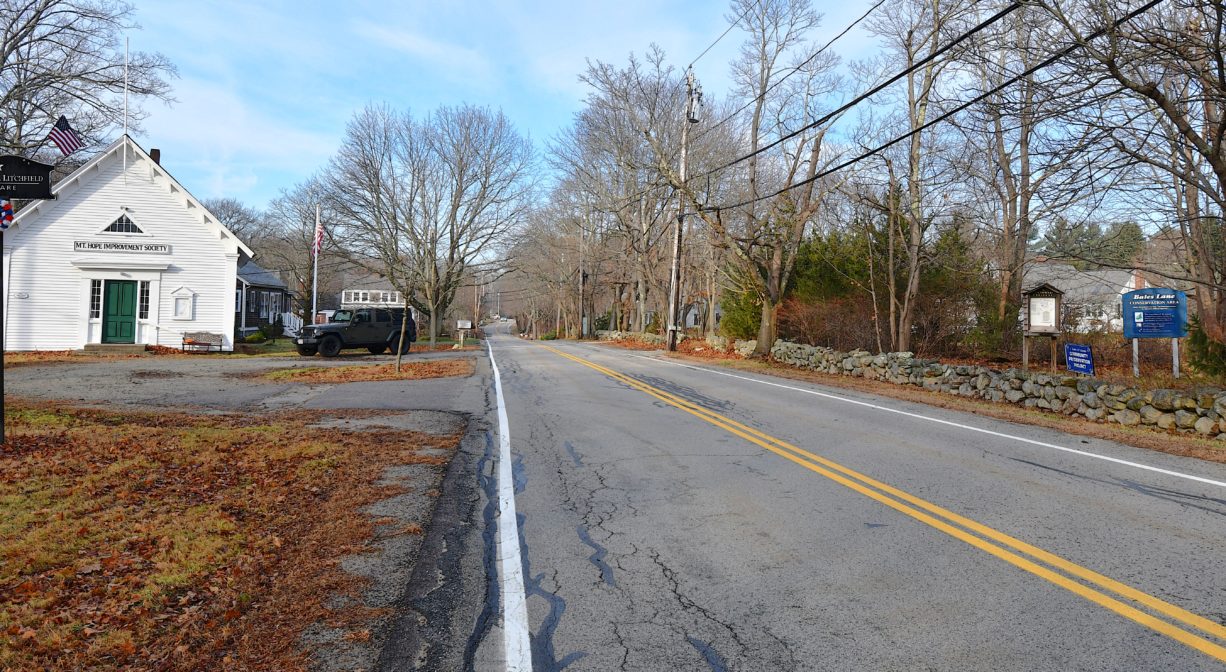 A photograph of a small white building at the edge of a road.