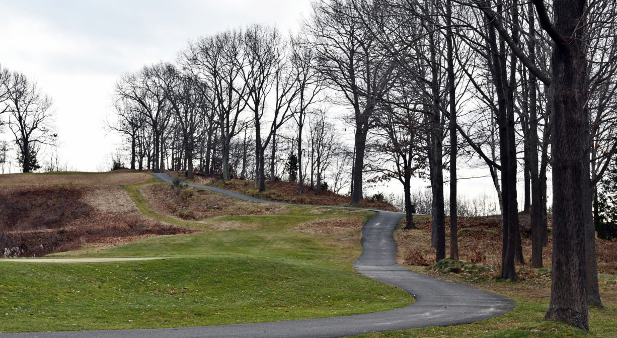 A photograph of apaved trail extending across a golf course with hills and trees.