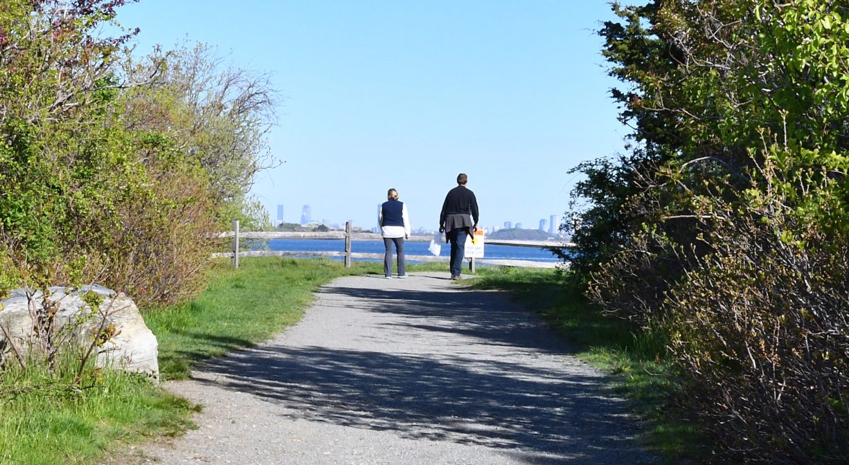 A photograph of two people walking a gravel trail toward the water.