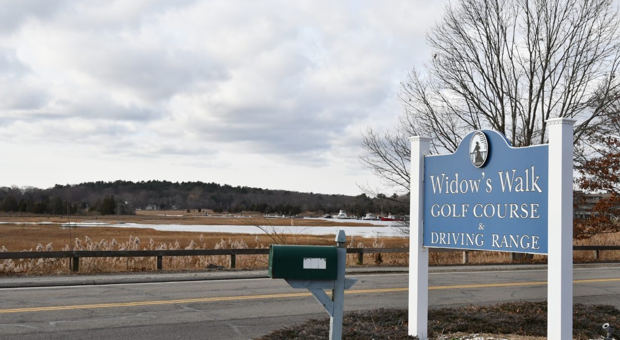 A photograph of a property sign beside a roadway with a salt marsh across the street.