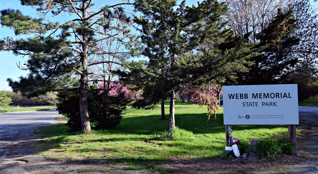 A photograph of a property sign beside a trail within a park.