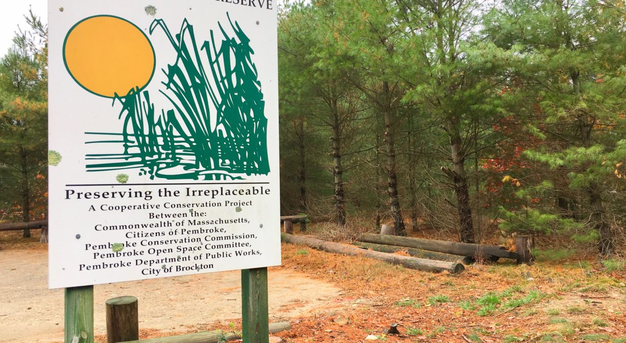 A photograph of a trail sign beside a parking lot.