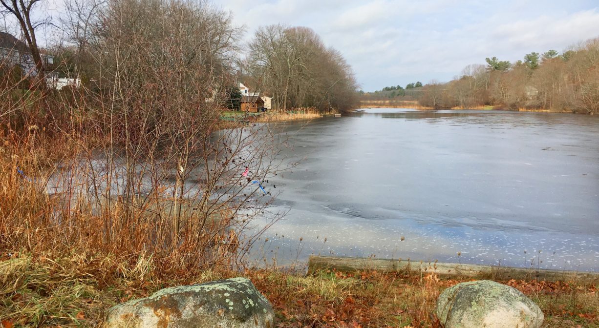 A photograph of a frozen pond with boulders in the foreground.