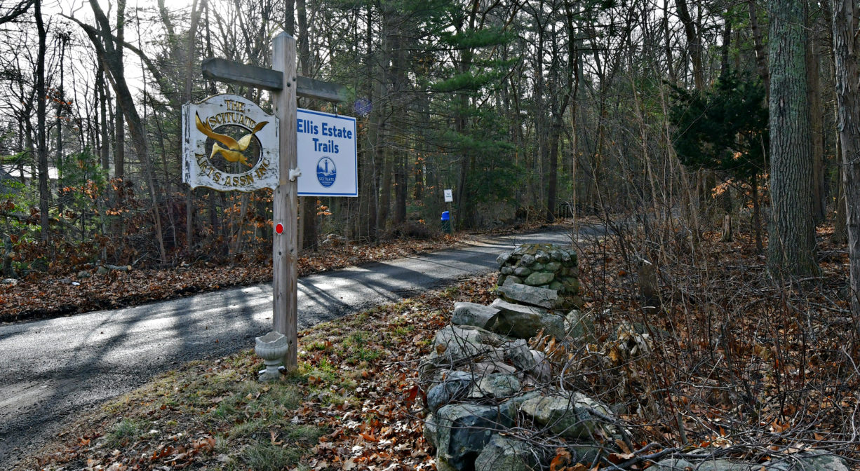 A property sign along a road with a stone wall and some trees.