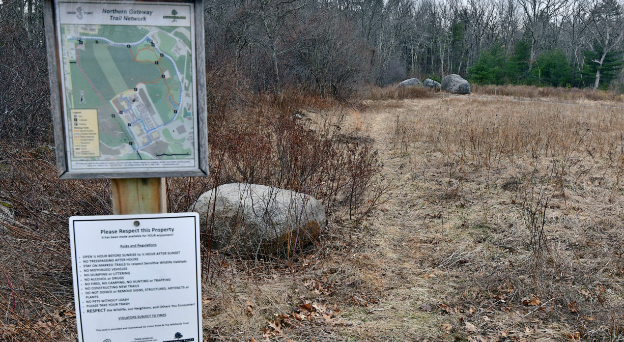 A photograph of a trailhead with a property sign.