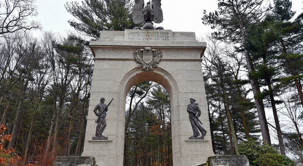 A photograph of a memorial archway with trees in the background.