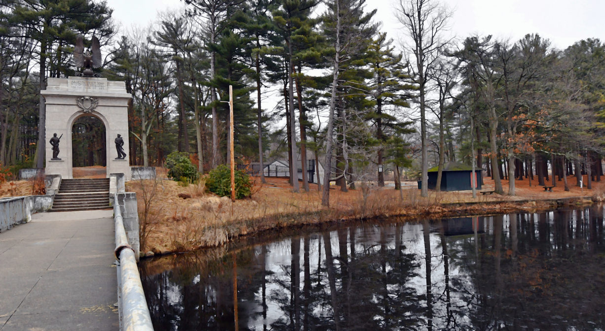 A photograph of a bridge over a pond with trees in the background.