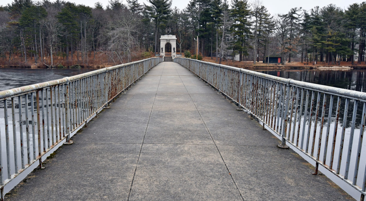 A photograph of a wide paved bridge over a pond.