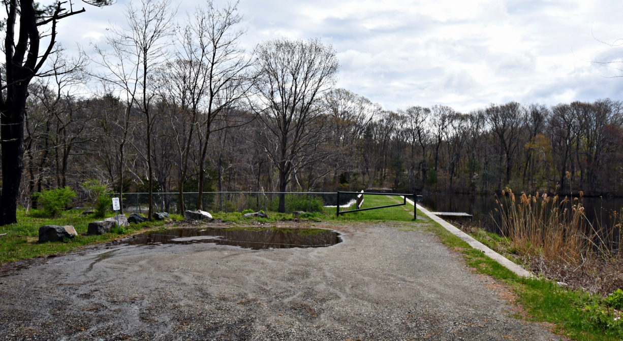 A photograph of an unpaved parking area beside a pond.