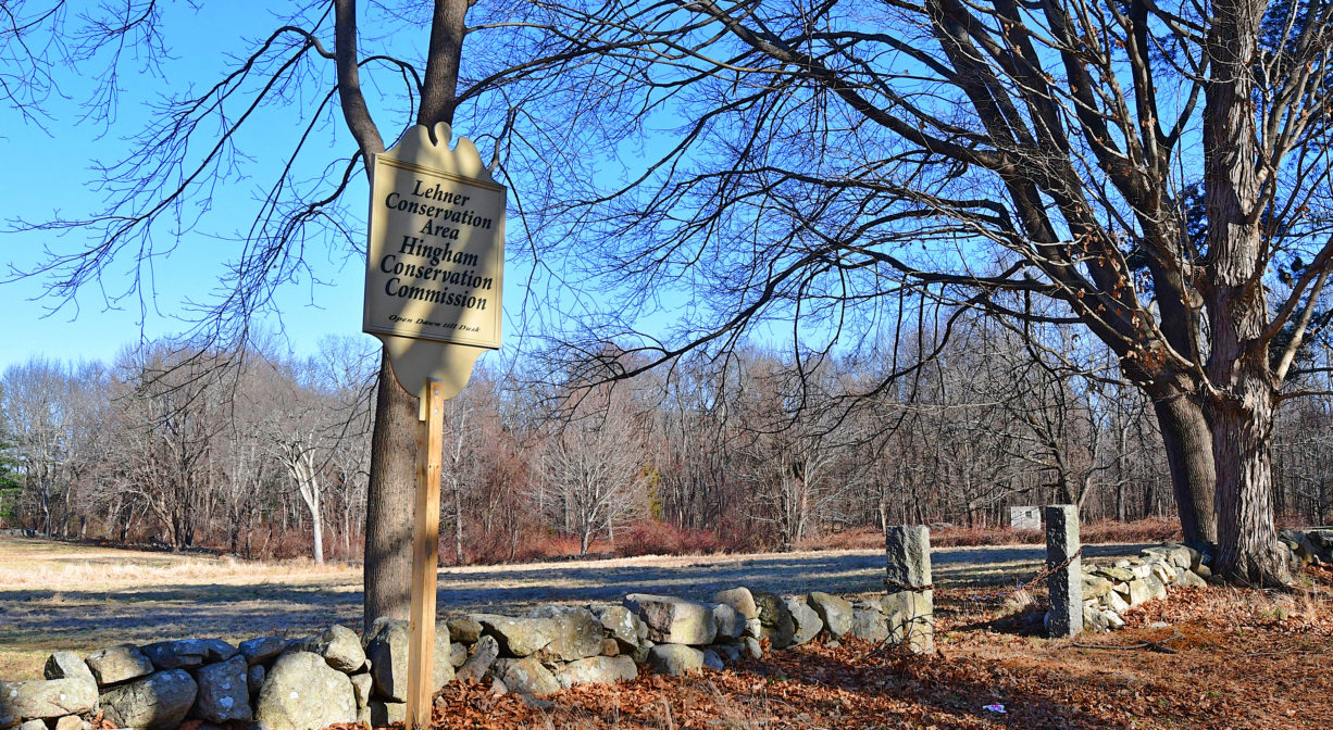 A photograph of a property sign beside a roadway, next to a stone wall.