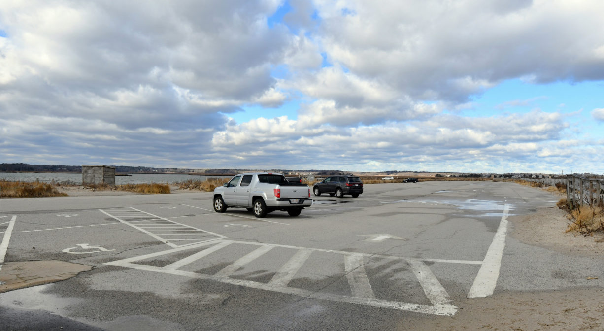 A photograph of a parking area with scattered vehicles, with a bay in the background.