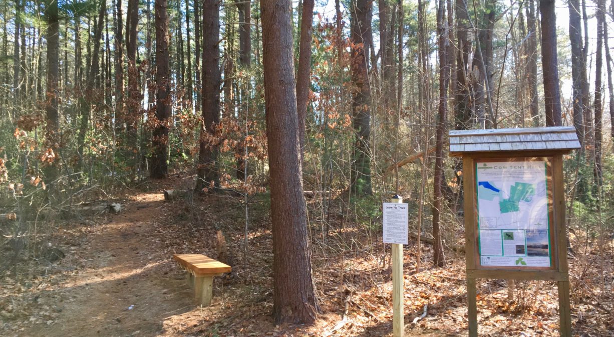 A photograph of a trail with a bench and some interpretive signage.