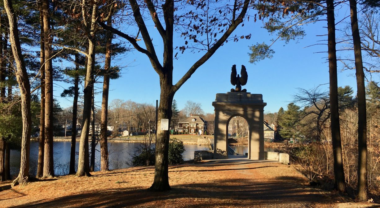 A photograph of a memorial archway on a pond in a wooded setting.