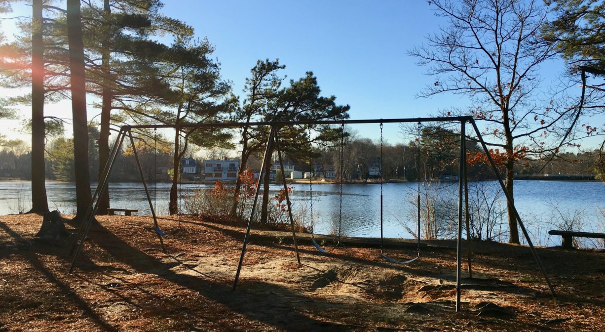 A photograph of a swing set beside a pond.