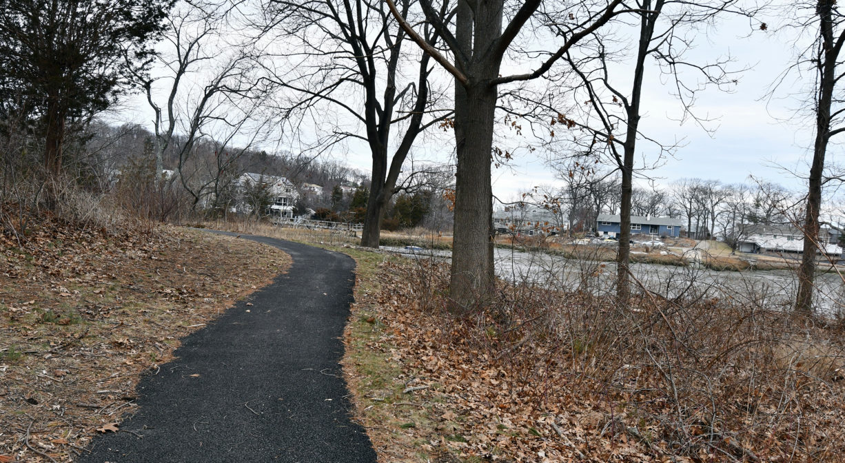 A photograph of a paved trail with a river in the distance.