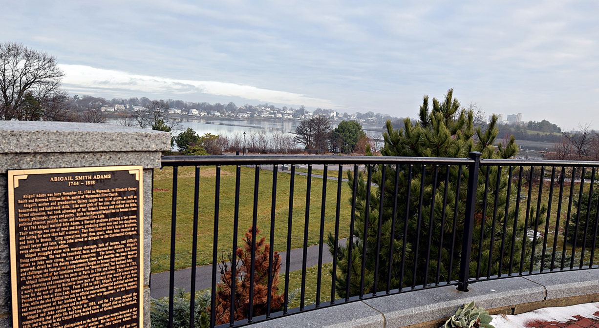 A photograph of a historic marker on a fence overlooking a park.