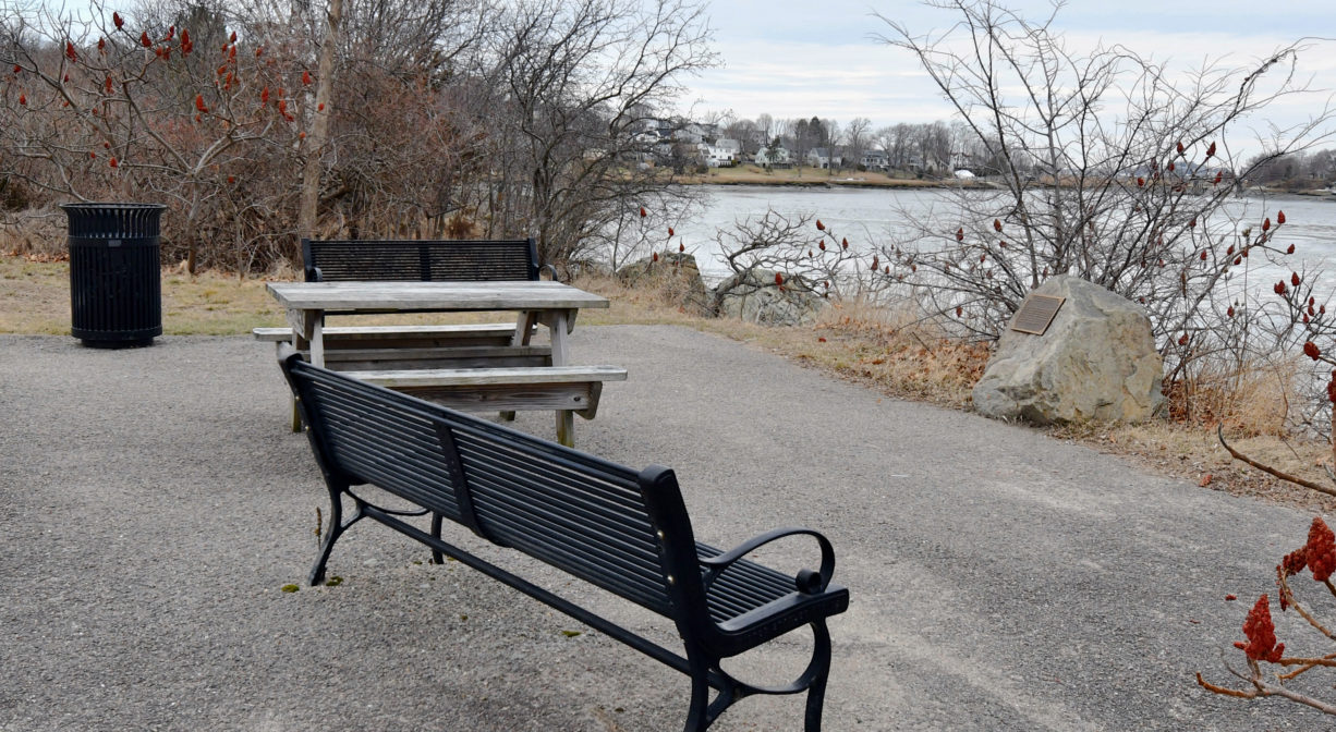 A photograph of a black bench overlooking a river.