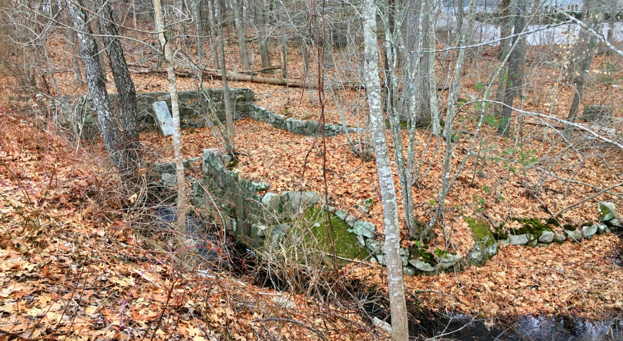 A photograph of a stream and an old mill foundation in a forest.